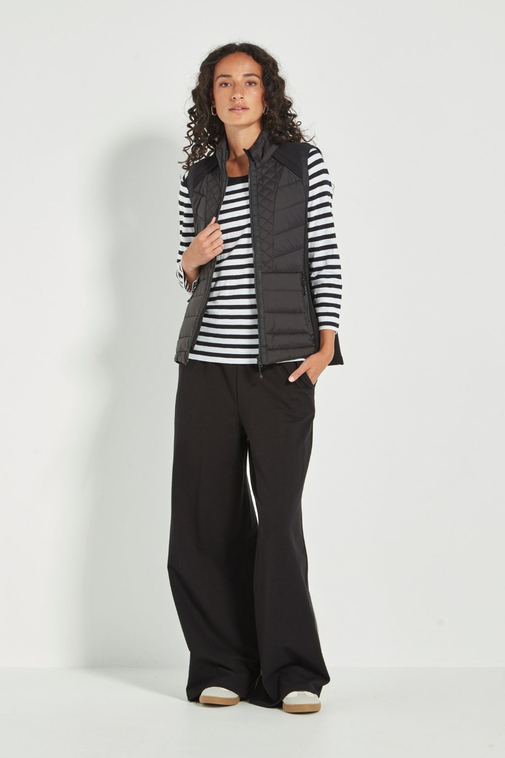 Woman wearing a striped shirt, black puffer vest, and wide-leg pants on a white background