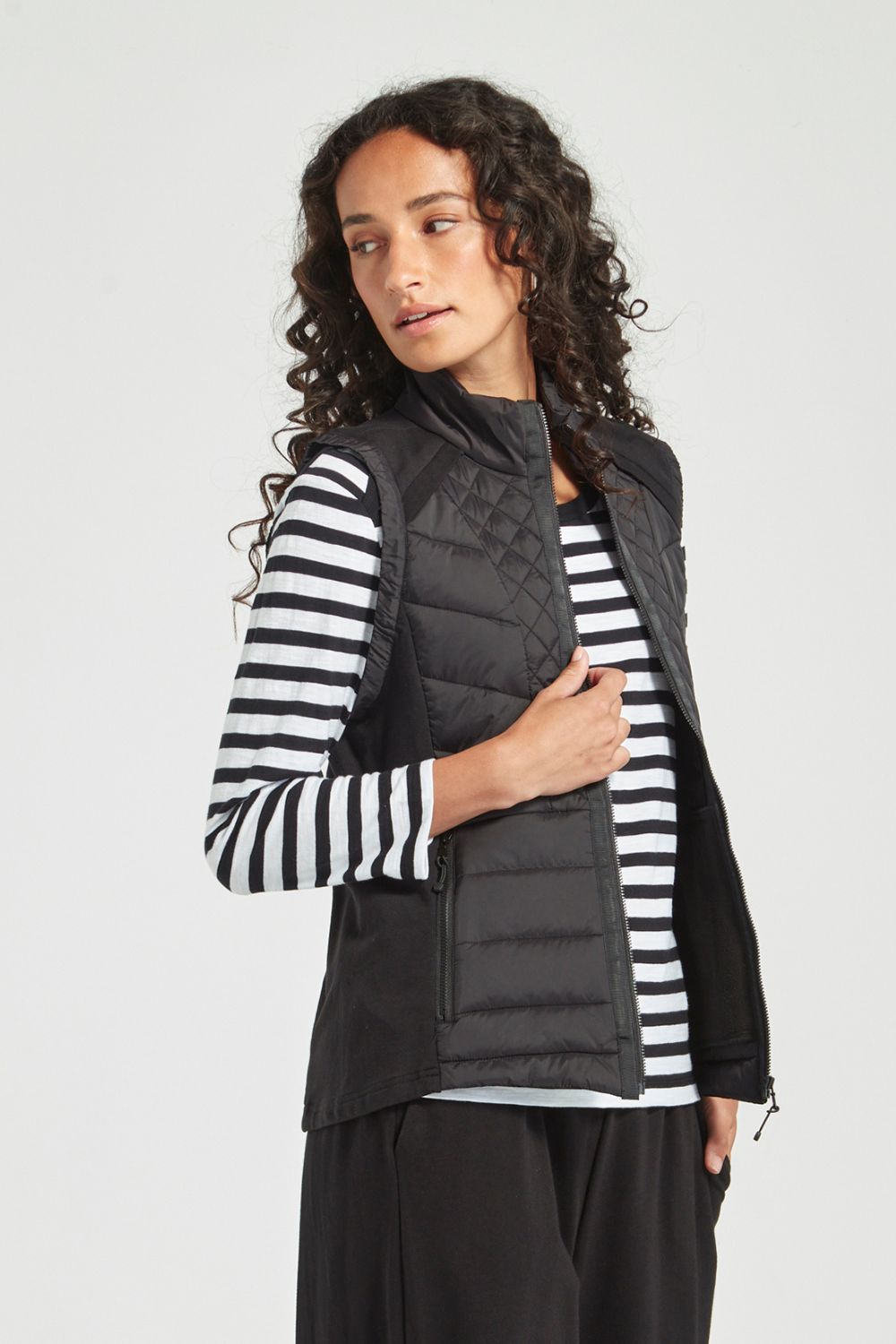 Woman wearing a black puffer vest over a striped shirt on a white background